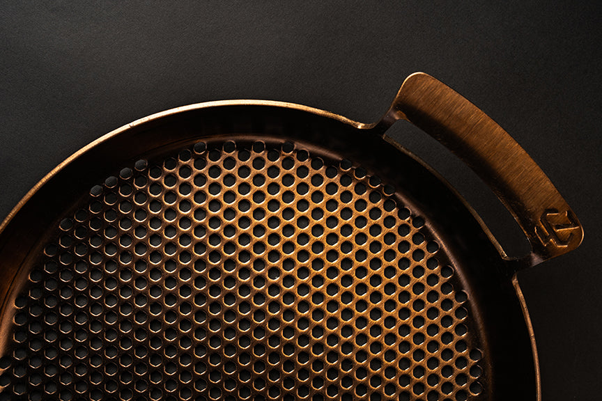Close-up of a bronze-colored metal mesh filter with a handle on a dark background
